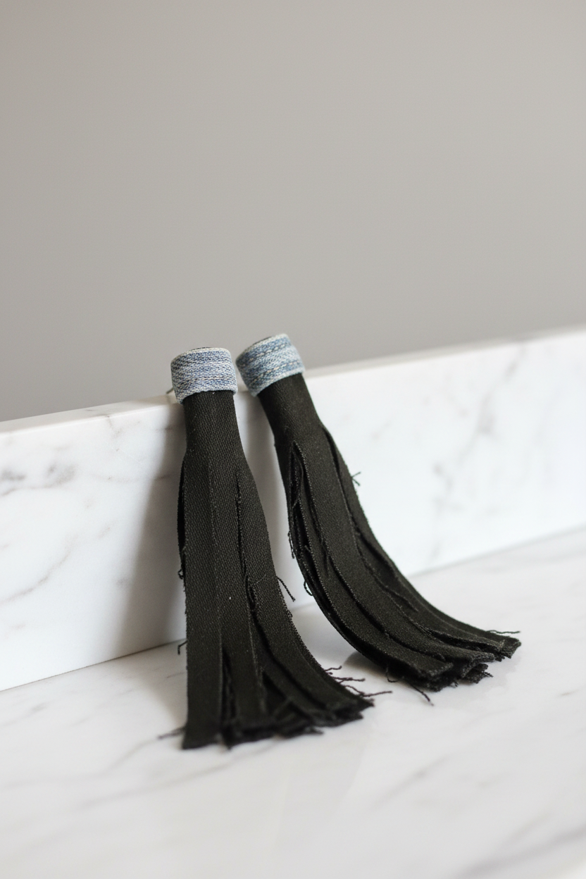 Midnight Denim Tassel Earrings with grey denim wrap top and dark olive-black fringe on polished marble background
