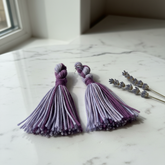 Lavender and plum two-tone twisted knot tassel earrings on white marble with dried lavender